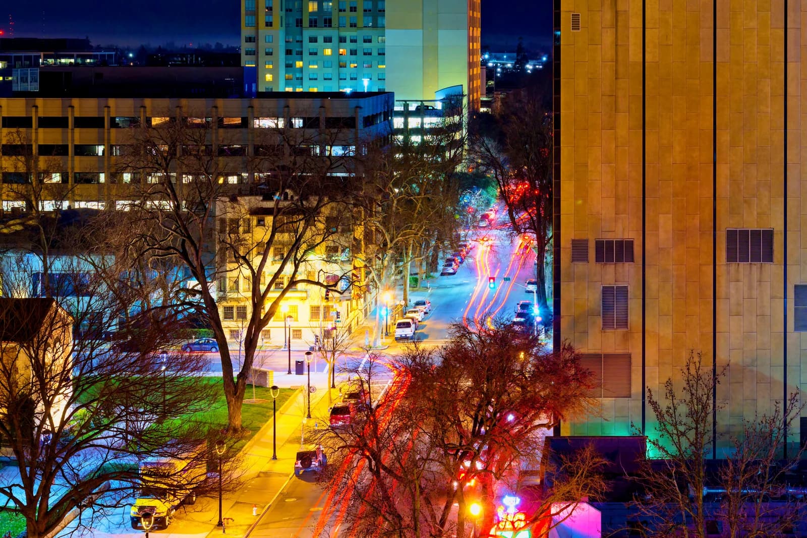 Calle de Midtown Sacramento iluminada de noche, con locales comerciales y árboles grandes.