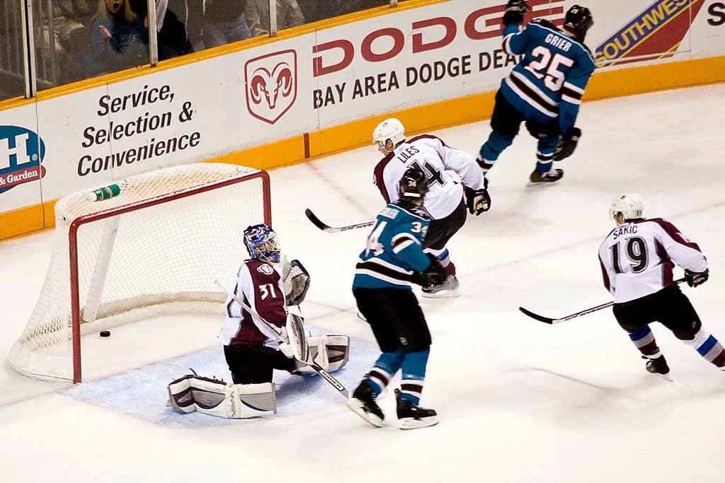 Mike Grier y un compañero de San Jose Sharks celebran un gol junto a la portería de Colorado Avalanche.