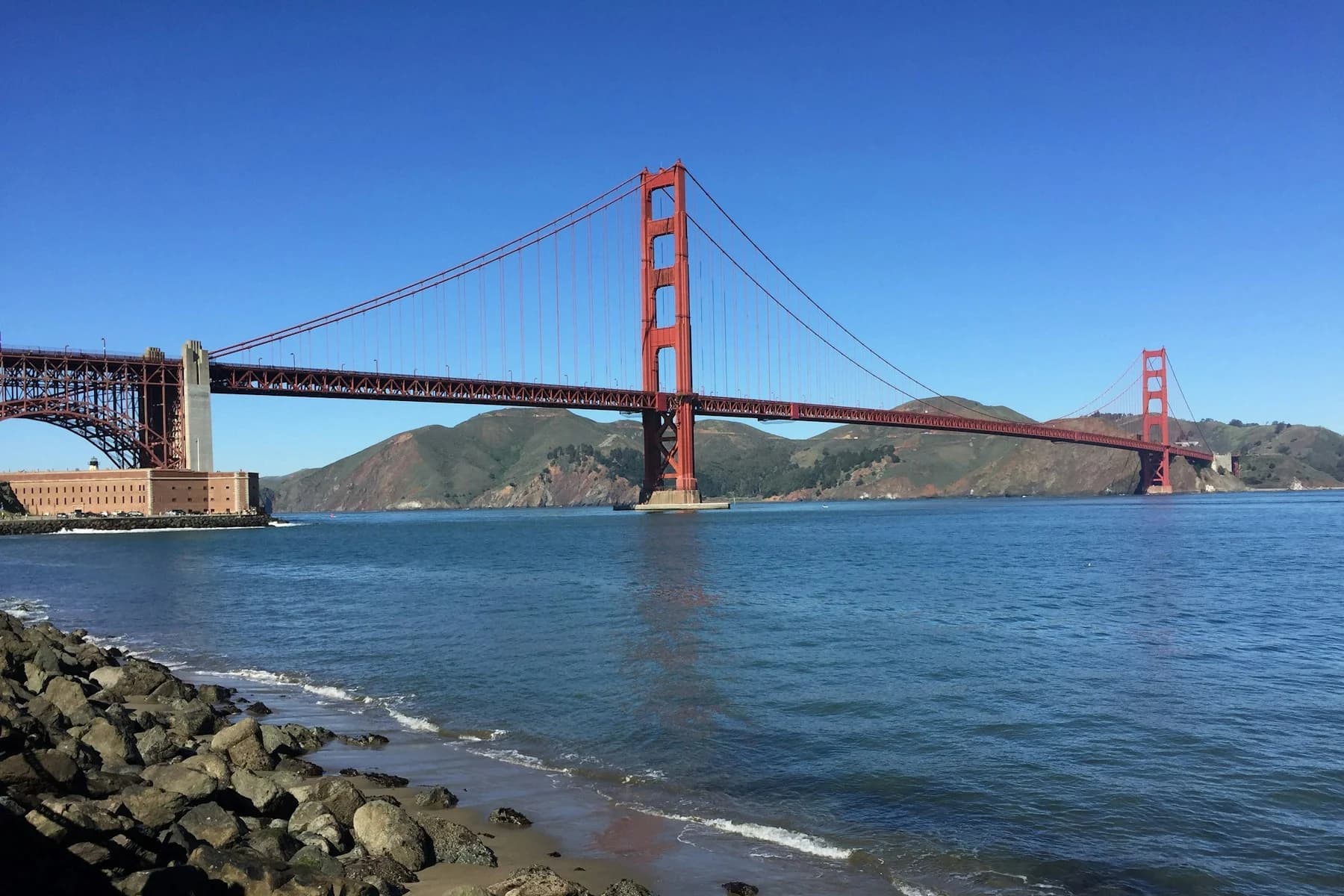 Red towers of the Golden Gate Bridge spanning blue bay water and the Marin hills