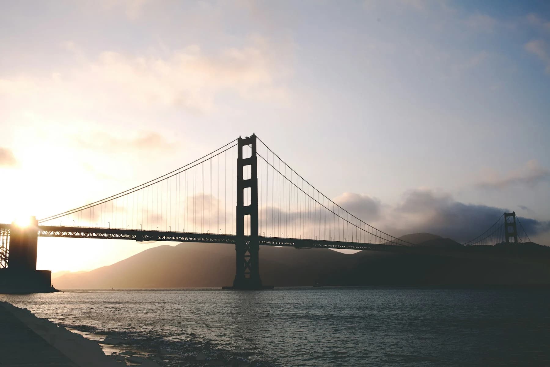 Golden Gate Bridge silhouetted against low sunlight and mist over the Marin hills