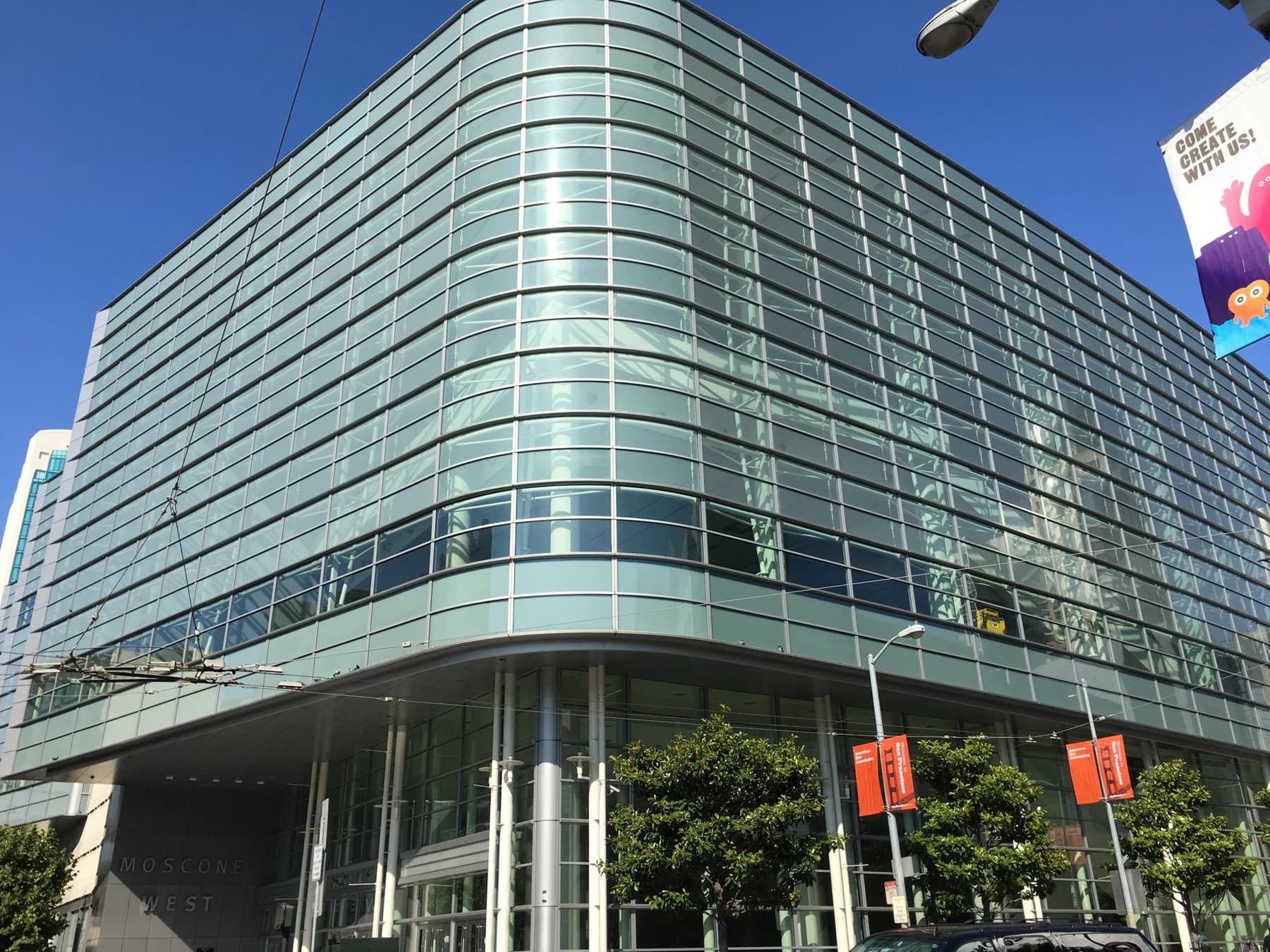 Fachada de vidrio y entrada de Moscone West iluminadas por el sol bajo un cielo azul despejado